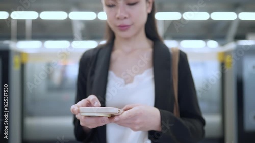 Asian city woman using cellphone while standing on the subway train platform, 5g cellular technology, urban lifestyle for new generation, smart technology wireless connection through smartphone