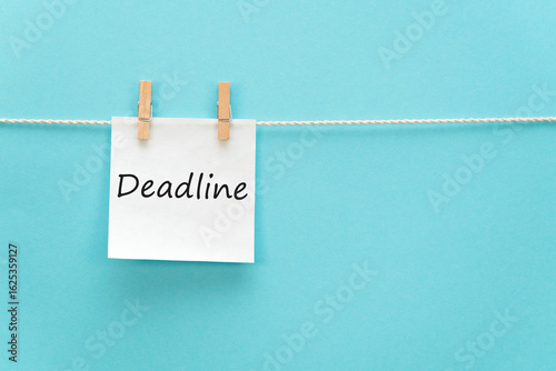 White sticker on a rope with a clothespin with an inscription - deadline. Blue background. No people.