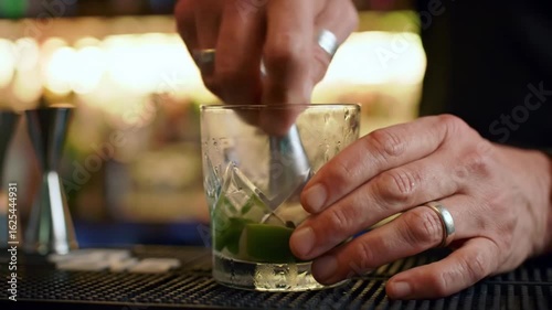 Bartender preparing a mojito cocktail with mint leaves and lime slices in a glass on a bar counter