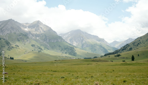 Tranquil green valley with majestic mountain range under cloudy sky