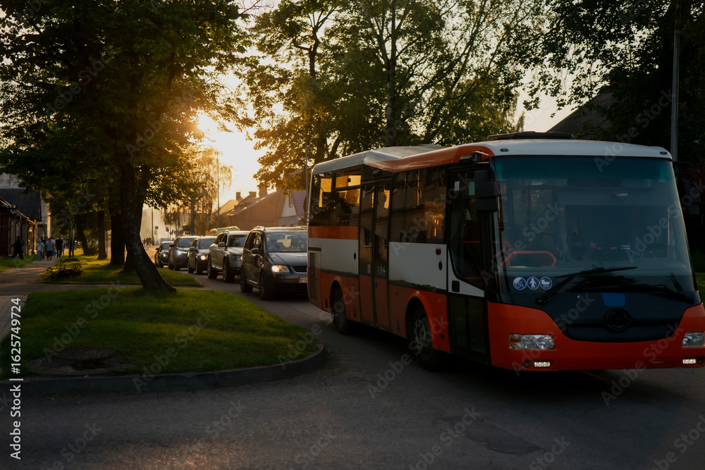 Fototapeta premium City bus and line of cars in residential neighborhood during golden hour, evening urban transportation scene with warm sunlight for traffic, public transit, mobility or commute concepts