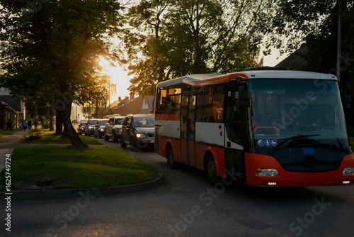 City bus and line of cars in residential neighborhood during golden hour, evening urban transportation scene with warm sunlight for traffic, public transit, mobility or commute concepts