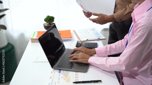 Team Collaboration with Computer: Two individuals engage in focused teamwork, with one typing on a laptop while another reviews documents, illustrating modern business synergy