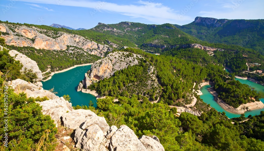 Turquoise lake winding through forested mountains, viewed from rocky cliffs under a blue sky Turquoise lake winding through forested mountains, viewed from rocky cliffs under a blue sky