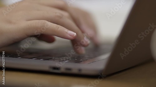 Close-up of young Asian woman's hands, early 20s, typing on laptop in library setting. Represents digital work, education, productivity, and remote study or freelance concepts.
