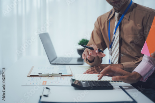 Meeting Financial Goals: Two focused colleagues engage in a collaborative analysis, deciphering intricate details on their journey toward reaching targets using a calculator.