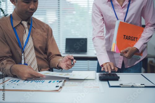 Teamwork on Target: A focused business pair collaborating in the office, analyzing data and crunching numbers, as they strategize to reach their TARGET goal.