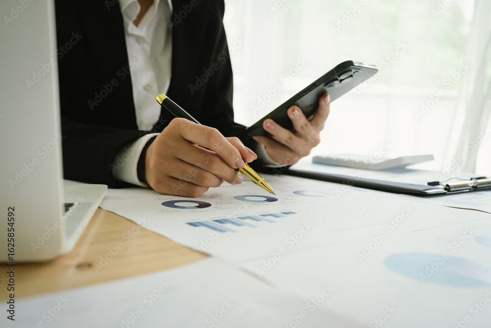 Fototapeta premium A business professional analyzes colorful financial charts and graphs on a desk, holding a pen and clipboard, representing planning, strategy, performance, and project management in the workplace.