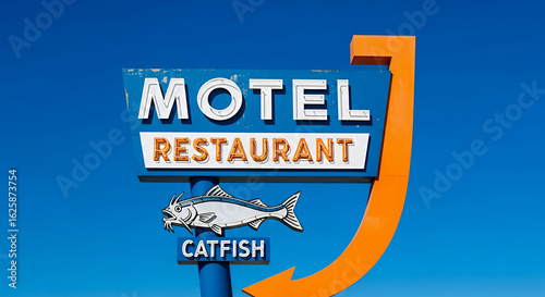 A retro motel and restaurant sign featuring a catfish illustration against a bright blue sky. The vintage signage suggests roadside travel and dining
