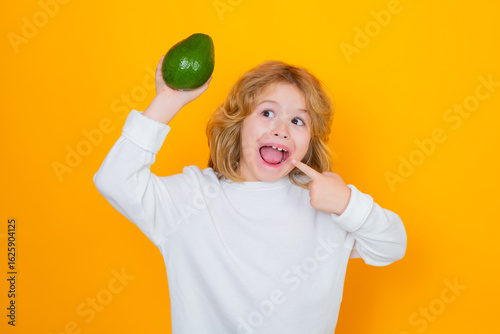 Kid hold red avocado in studio. Studio portrait of cute child with avocado isolated on yellow background.