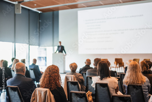 Speaker giving a talk in conference hall at business event. Rear view of unrecognizable people in audience at the conference hall. Business and entrepreneurship concept
