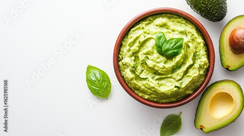 A vibrant bowl of fresh guacamole garnished with basil leaves, accompanied by sliced avocados on a clean, white background.