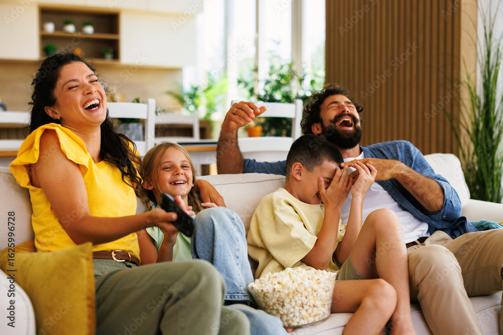 Obraz premium Happy family watching comedy on tv and laughing together on sofa