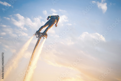 A flyboard athlete hovers over the water against the sunset sky, propelled by powerful jet streams of water. Flyboarding adventure at sunset over calm waters showcasing an exhilarating water sport