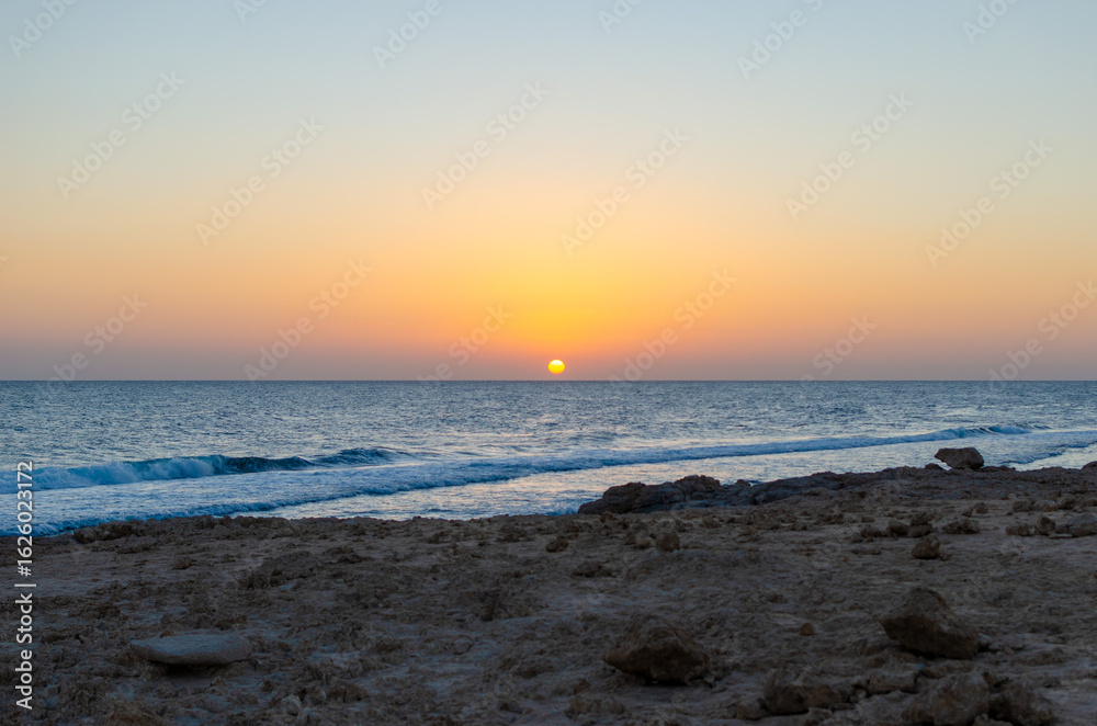 Fototapeta premium Sunset over the sea with orange sky and beach rocks in Egypt