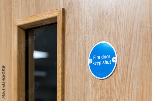 Close-up of a typical Fire Door Keep Shut sign seen on an interior door within a British hospital. The firedog prevents any fire or smoke spreading in the building.