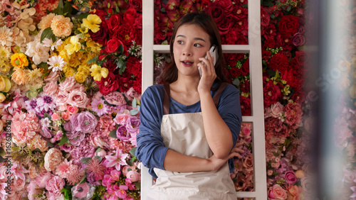 Schilderij op canvas Asian business owner managing flower shop orders using mobile phone customer com