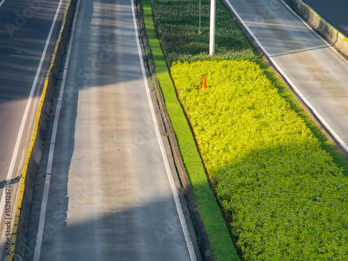 Photos Top view of a clean, empty urban road with a green median strip and traffic cone, highlighting city infrastructure, landscaping, and transportation design