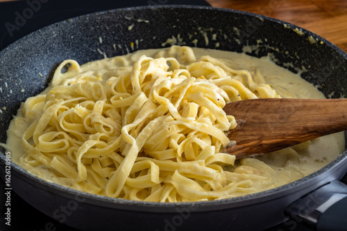 Cooking creamy chicken alfredo fettuccine pasta in frying pan