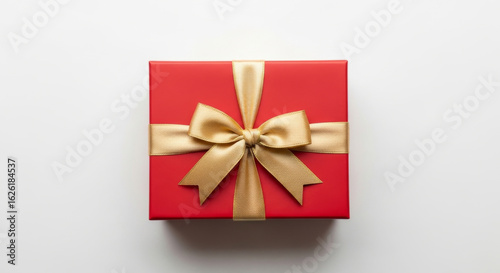 A red gift box with a gold ribbon and bow sitting on a white surface from an overhead perspective