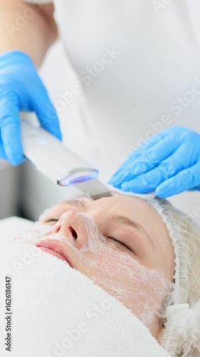 Ultrasonic facial cleansing procedure in beauty salon – professional deep skin cleaning with device, vertical and horizontal video for cosmetology, skincare and spa treatments.