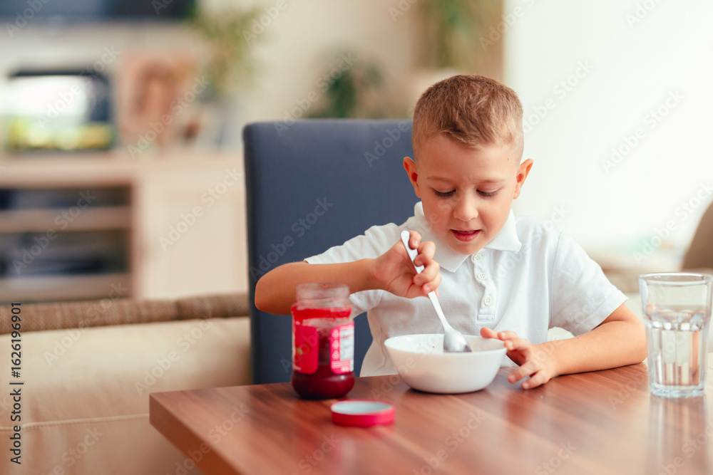 Cute 5-year-old boy having breakfast at home, eating porridge with jam. Cute 5-year-old boy having breakfast at home, eating porridge with jam.