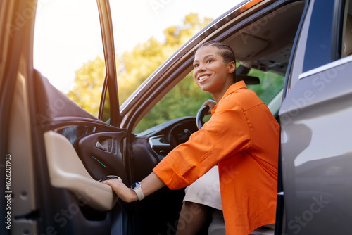 Smiling young black woman exiting car, holding door and looking away. Positive vibe, freedom and anticipation captured in motion, closeup shot