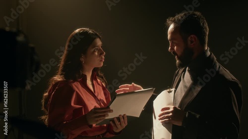 Pleased filming director giving his feedback to young actress after passing her acting auditions in dimly lit studio