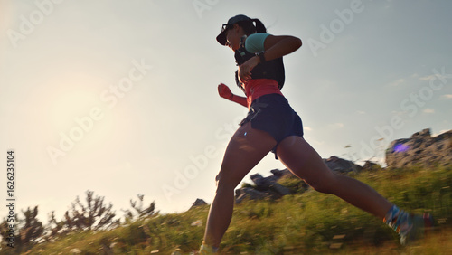 Determined female runner in athletic gear sprints across a grassy hillside, long exposure capturing sunset's warm glow, highlighting endurance, perseverance, and joy in cross-country running.