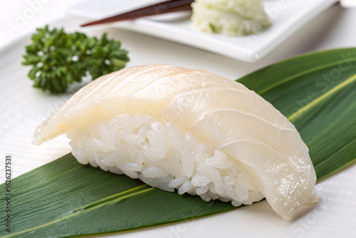 White fish sushi nigiri on bamboo leaf with wasabi, pickled ginger garnish, and traditional Japanese presentation on white plate.
