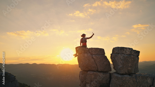 Quadro su tela Triumphant runner celebrates atop a rugged cliff at sunset, golden sky and distant mountains highlighting endurance and joy in this breathtaking outdoor scene