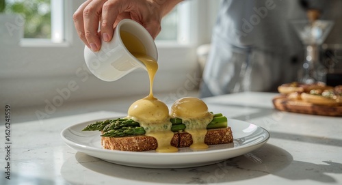 Wallpaper Mural Pouring hollandaise sauce over eggs benedict with asparagus on toast in a bright kitchen setting Torontodigital.ca