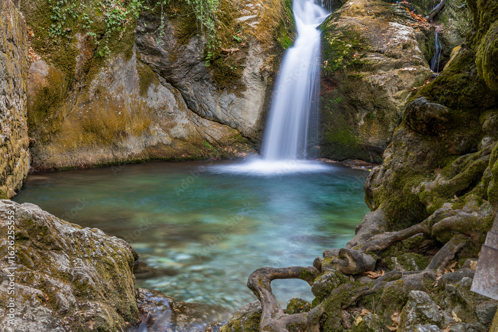 Fototapeta premium Close-up view of a vibrant turquoise pool and flowing waterfall surrounded by rocks and tree roots in Ayazma Nature Park, Bayramiç, Çanakkale, Turkey