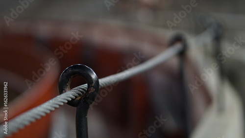 Close-up of thick cable and metallic supports over red seats in a bullring arena with neutral lighting