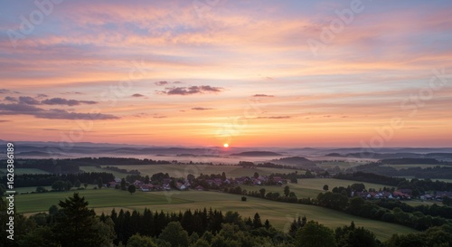 Pastel Sunrise Over a Tranquil Village Nestled in a Misty, Rolling Landscape.