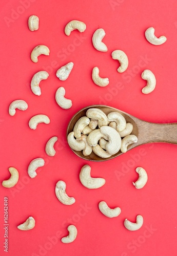 Top View of Cashew Nuts in a Wooden Spoon Isolated on Red Background with Copy Space in Vertical Orientation, Healthy Eating Dry Fruit