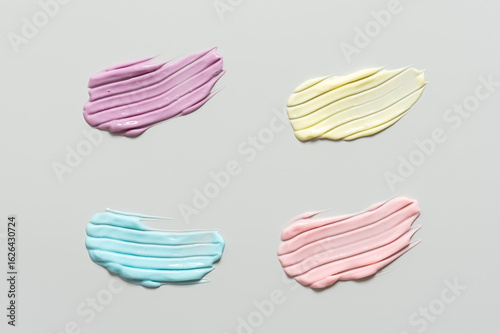 Colored smears of cosmetic cream on gray pastel background, colorful cream samples with striped pattern, cosmetic banner, top view