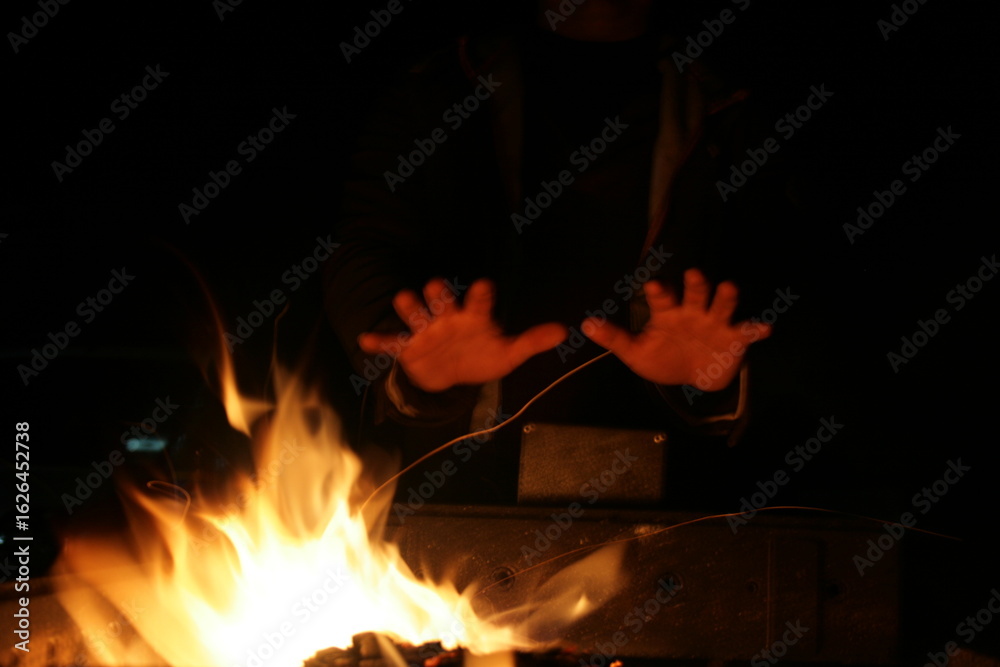 Fototapeta premium Warm glow of flames dances in the night as hands reach out for comfort and connection by the fire