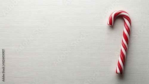 A single red and white candy cane rests on a textured white surface, offering a simple yet festive visual for holiday designs