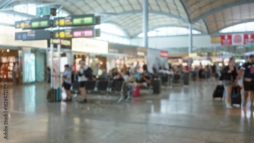 Busy airport terminal with blurred travelers walking, waiting, and using devices under large signs, capturing the bustling environment of modern air travel