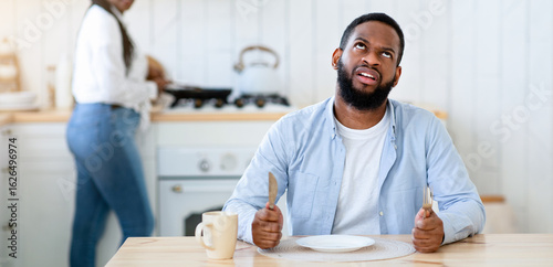 Fényképezés Impatient hungry black husband waiting for dinner with empty plate, bored starvi