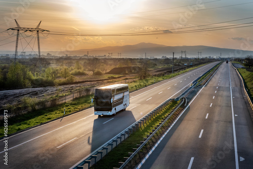 Modern white bus traveling on a wide sunset highway with a beautiful dramatic sky. Highway transportation of passengers on a highway