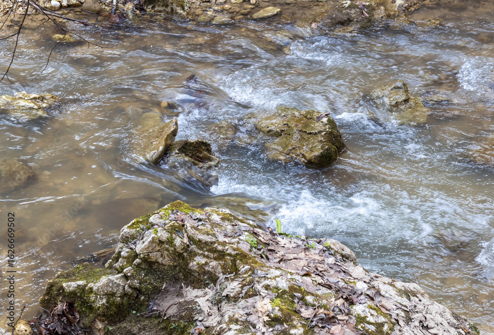 A shallow riverbed with an exposed rocky bottom , a small stream and a stream of water, the spring period in nature A shallow riverbed with an exposed rocky bottom , a small stream and a stream of water, the spring period in nature