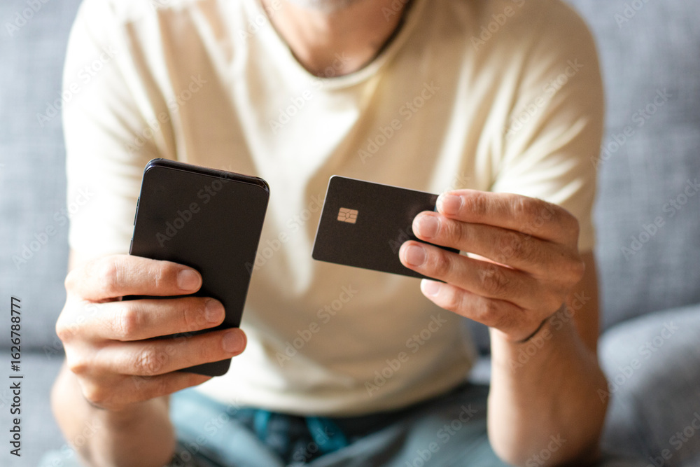 Close-Up of Man Holding Credit Card and Smartphone at Home on Sofa Close-Up of Man Holding Credit Card and Smartphone at Home on Sofa