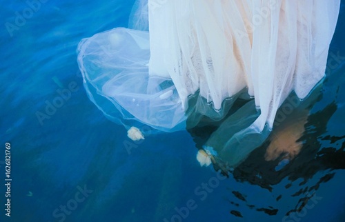Frau mit langem weißen Hochzeitskleid steht in blauem Flusswasser in der Natur am Abend im Sommer