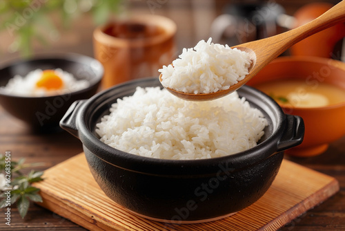 Steaming White Rice Transferred from Black Clay Pot to Bowl with Wooden Spoon in Japanese Kitchen
