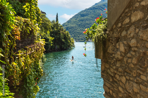 Fototapeta Naklejka Na Ścianę i Meble -  View of Ponte del lago, Nesso on Lake Como in Italy. Man paddling on a paddleboard Lake Como on a sunny summer day