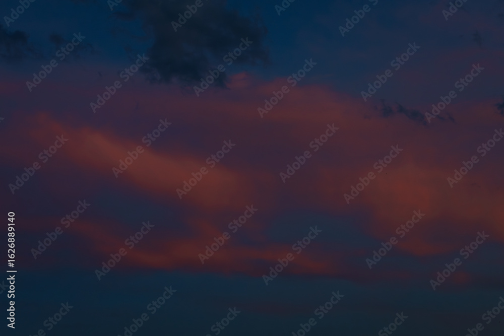Fototapeta premium Scattered dark clouds float across a twilight sky bathed in deep blue and delicate pink tones, creating a peaceful and moody scene with copy space.