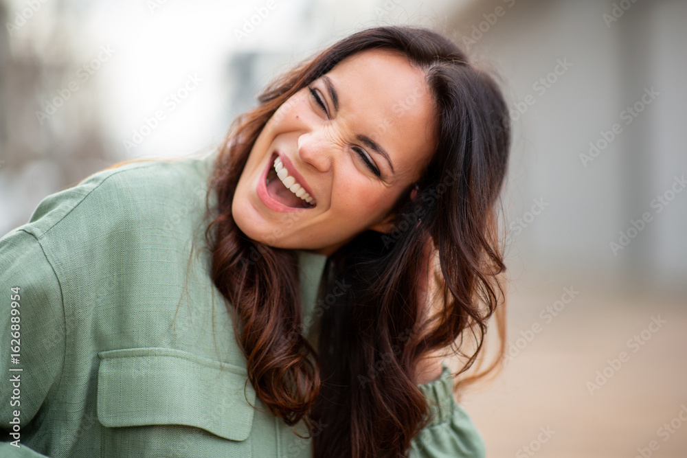 Fototapeta premium Playful woman in green jacket laughing joyfully outdoors