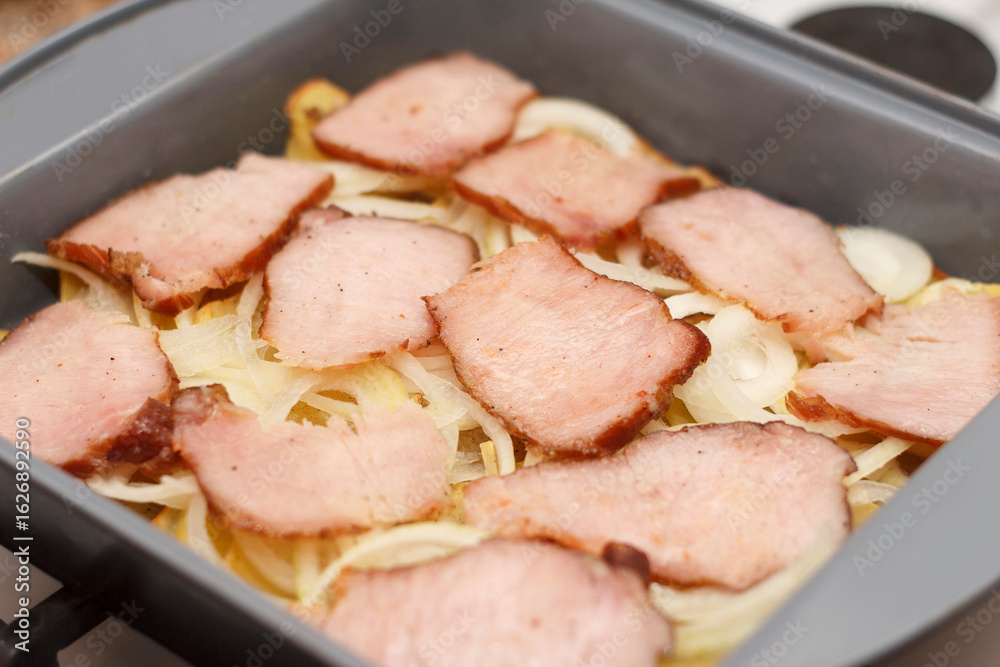 Sliced ham on a bed of potatoes and onions in a baking dish. Dish is ready for cooking Sliced ham on a bed of potatoes and onions in a baking dish. Dish is ready for cooking